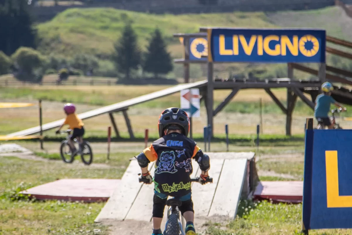 Bambino in bicicletta su un percorso a Livigno con sfondo boscoso.