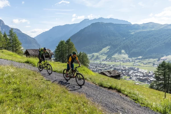Due ciclisti pedalano lungo un sentiero di montagna con viste panoramiche sulla valle sottostante.