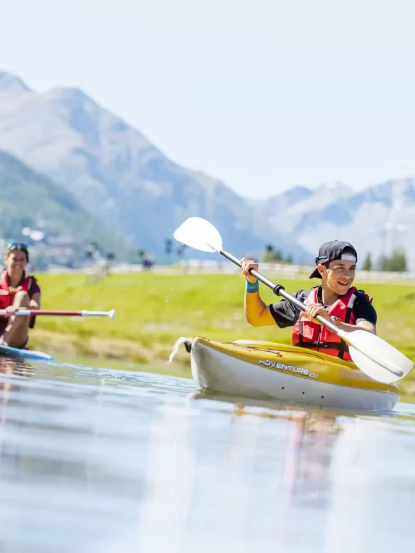 Due persone in kayak su un lago di montagna durante una giornata di sole.