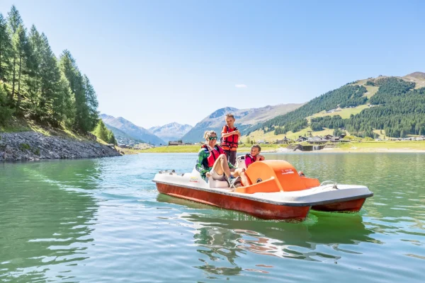 Una famiglia in pedalò su un lago montano circondato da foreste e montagne.