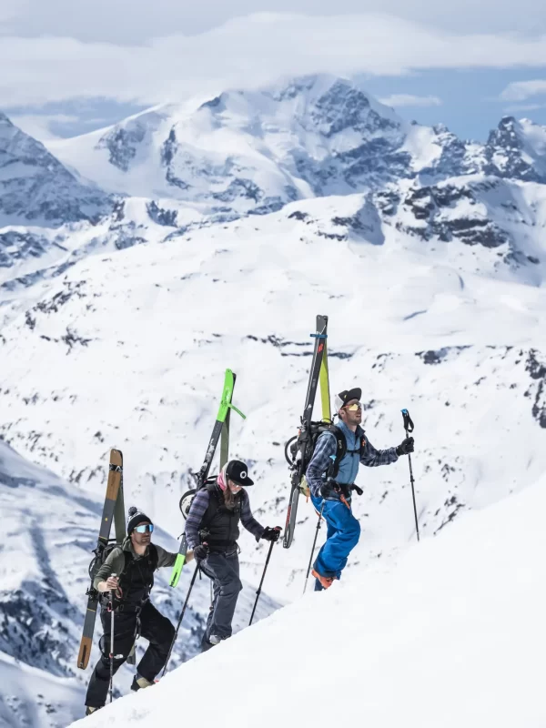 Tre persone scalano una montagna innevata con gli sci sulle spalle.