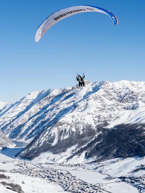 Persona in parapendio sopra paesaggio alpino innevato.