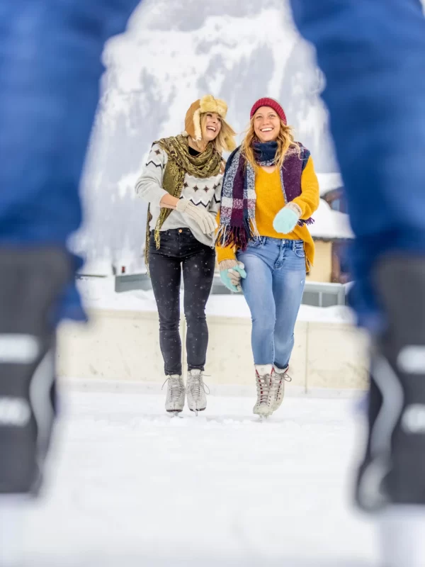 Due persone felici che pattinano su ghiaccio all'aperto in un paesaggio innevato.