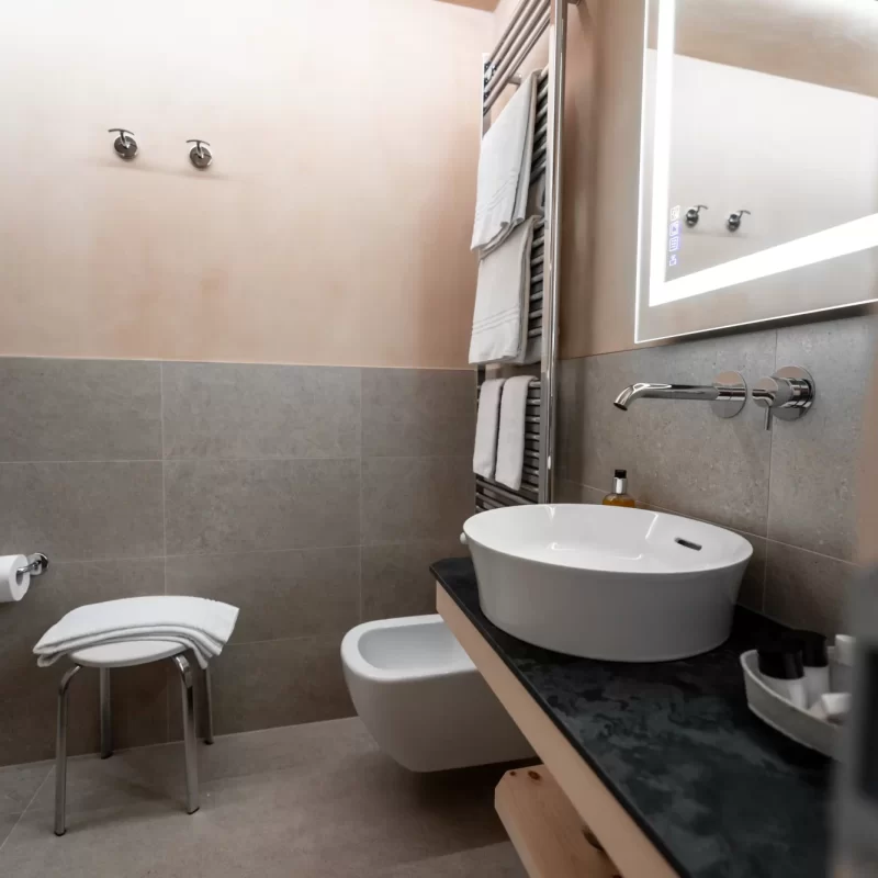 Modernes Badezimmer mit weißem Waschbecken, beleuchtetem Spiegel und Handtuchwärmer.