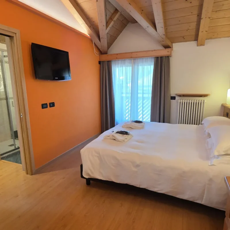 Gemütliches Hotelzimmer mit Doppelbett, Holzbalkendecke und angrenzendem Bad.