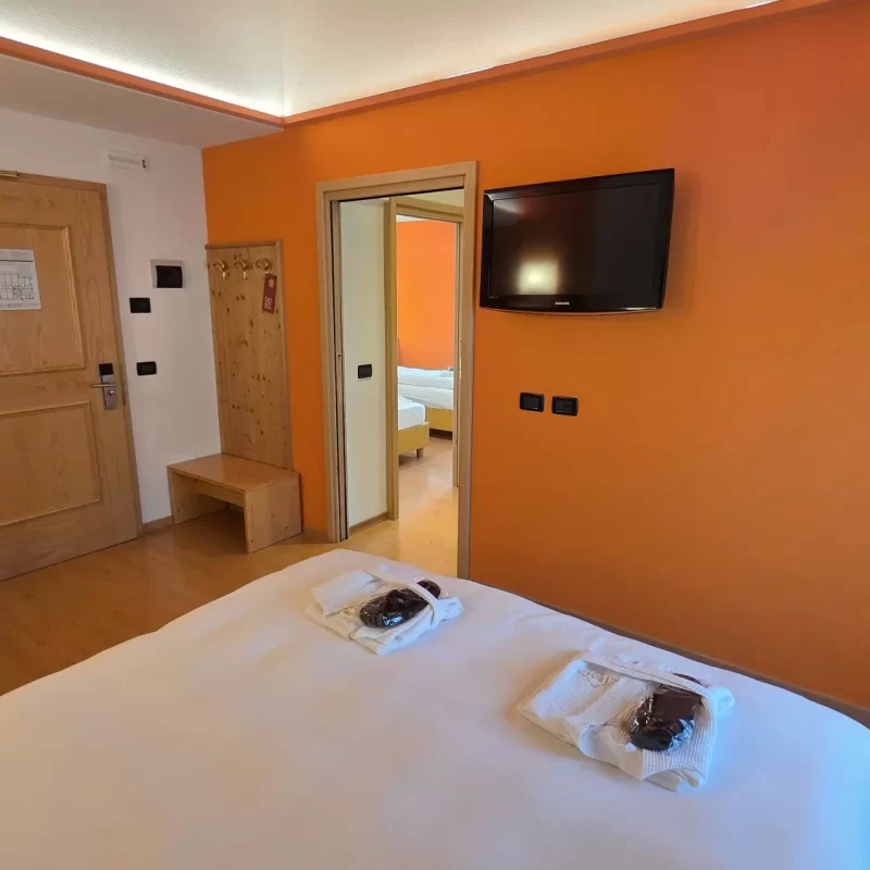 Hotelzimmer mit orangefarbenen Wänden, Doppelbett und an der Wand befestigtem Fernseher.