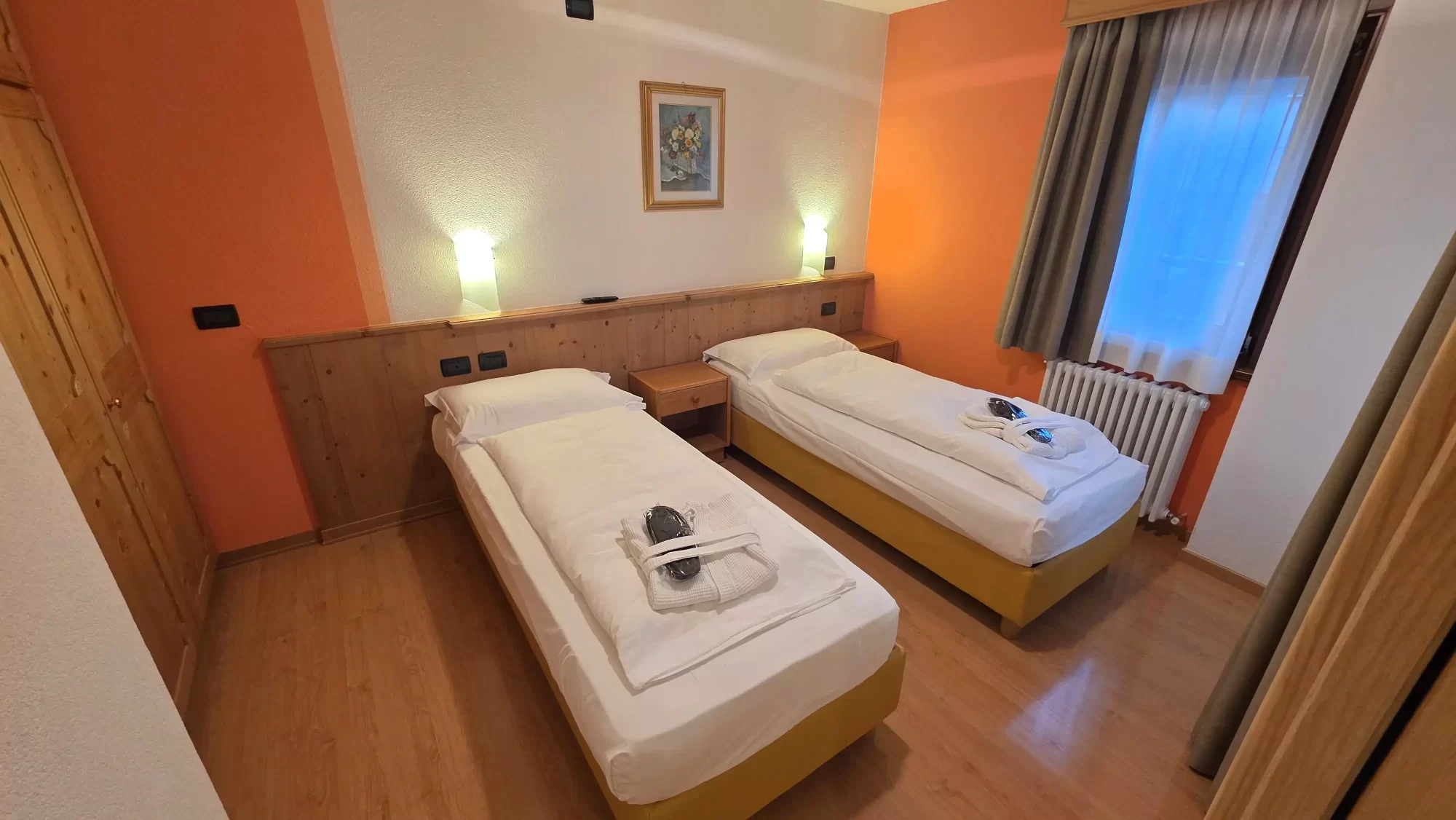 Camera con due letti singoli, pareti arancioni e arredamento in legno.