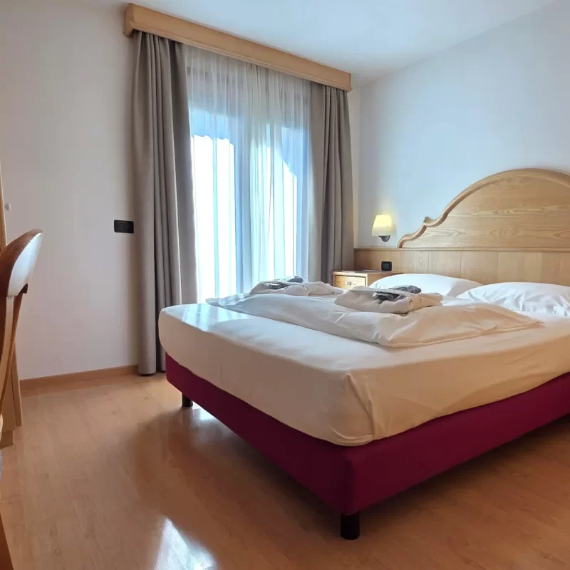 Gemütliches Hotelzimmer mit Doppelbett, Holzmöbeln und großem Fenster mit Vorhängen.