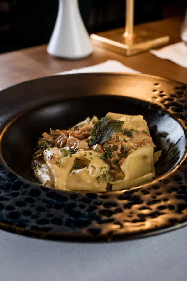Piatto di pasta fresca condita con salsa cremosa e funghi, servita in un piatto elegante.