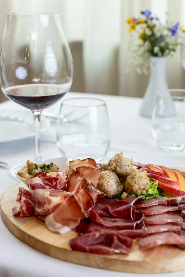 Tagliere di salumi e formaggi con calice di vino rosso su tavola elegante.