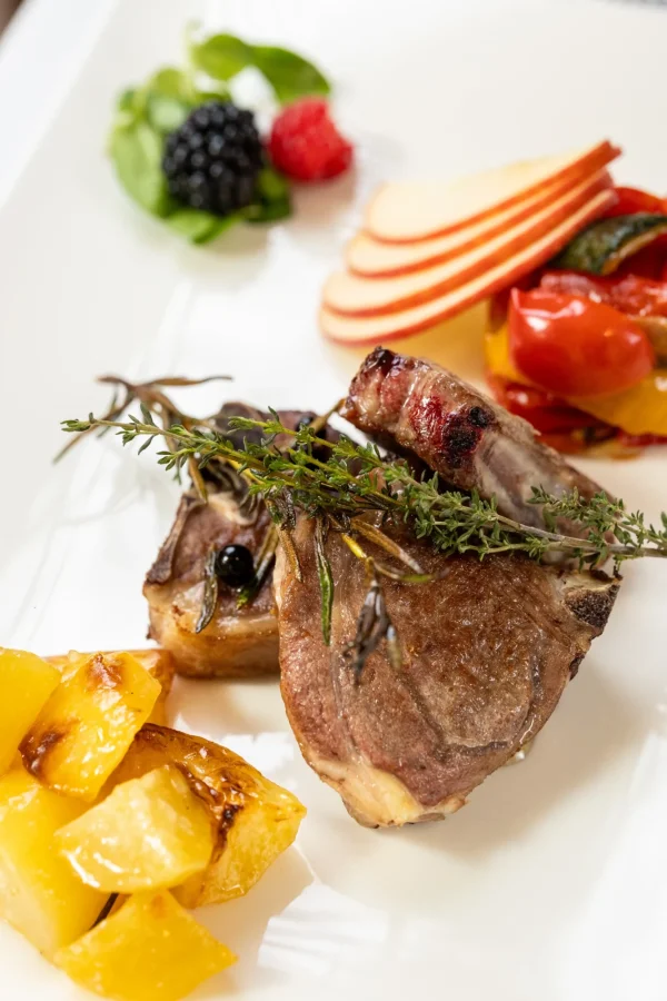 Piatto gourmet con costolette d'agnello, patate, frutta e verdure.