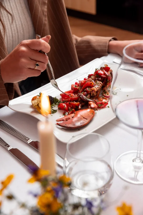 Persona che gusta un piatto di aragosta con pomodori ed erbe aromatiche a lume di candela.