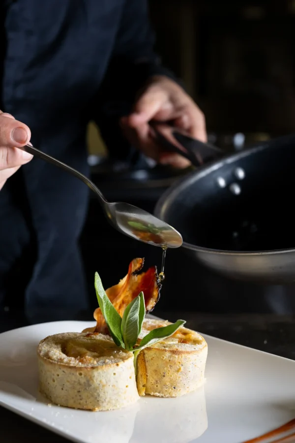 Un cuoco versa una salsa su un piatto raffinato con decorazione di salvia.