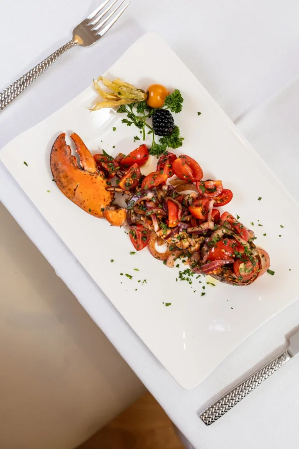 Piatto di astice con pomodorini e cipolle su un tavolo apparecchiato.