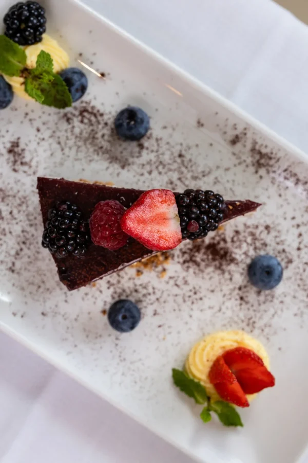 Fetta di torta al cioccolato con frutti di bosco freschi su un piatto decorato.