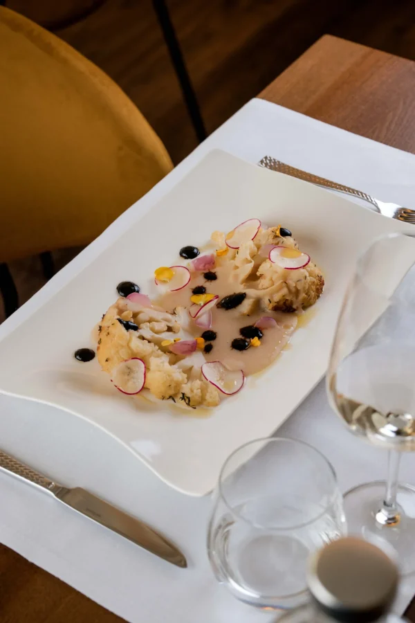Piatto gourmet con cavolfiore e decorazioni su tavola apparecchiata.