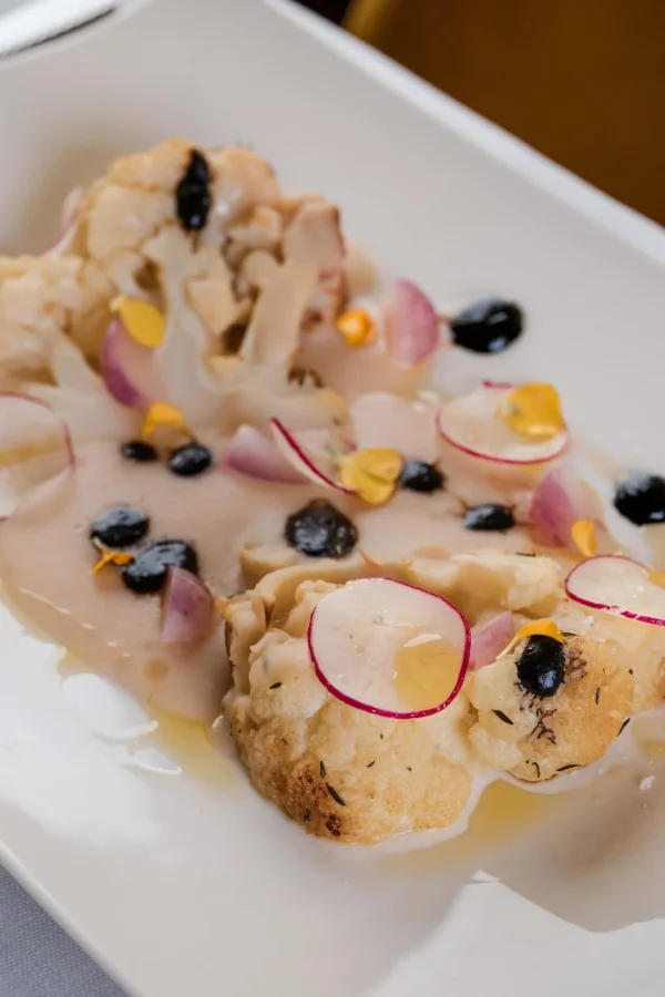 Un piatto di cavolfiore arrostito con fette di rapanello, salsa cremosa e gocce di olio.