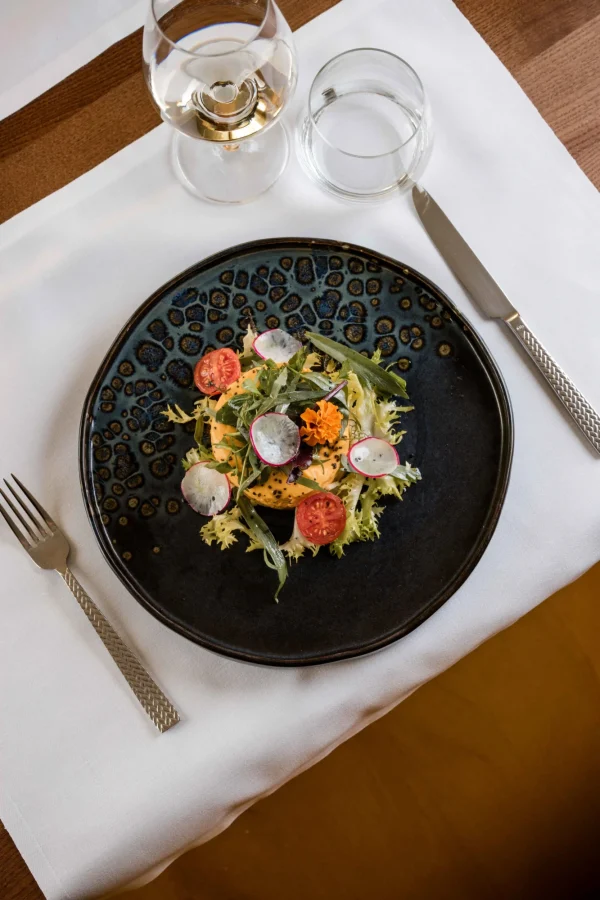 Piatto di insalata gourmet con pomodori e ravanelli su tavola apparecchiata.