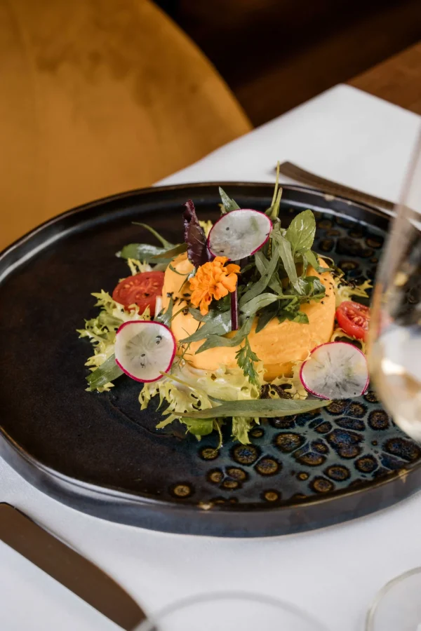 Piatto di mousse con decorazione di verdure e fiori su un piatto scuro.