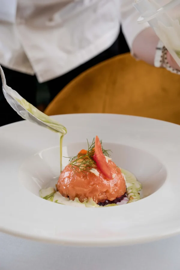 Chef che completa un piatto gourmet con una salsa cremosa.