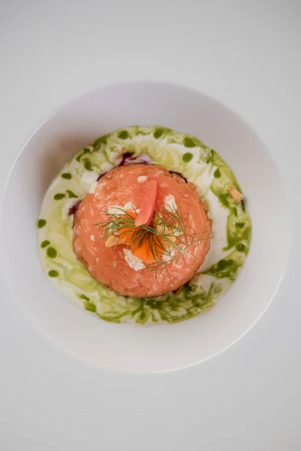 Piatto gourmet con tartare di salmone decorata con erbe fresche e salse colorate.
