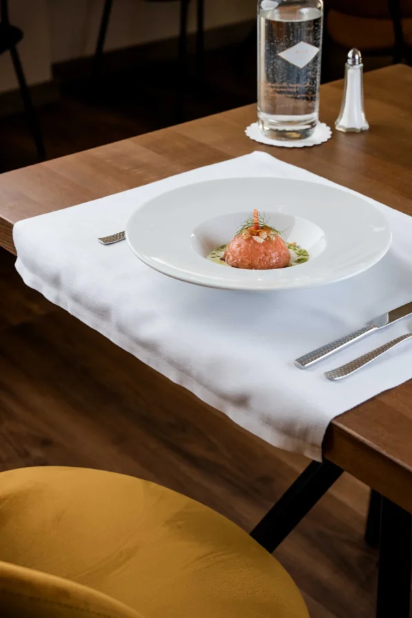 Piatto di tartare di salmone su tovagliolo bianco, con posate eleganti, bottiglia d'acqua e saliera sul tavolo.