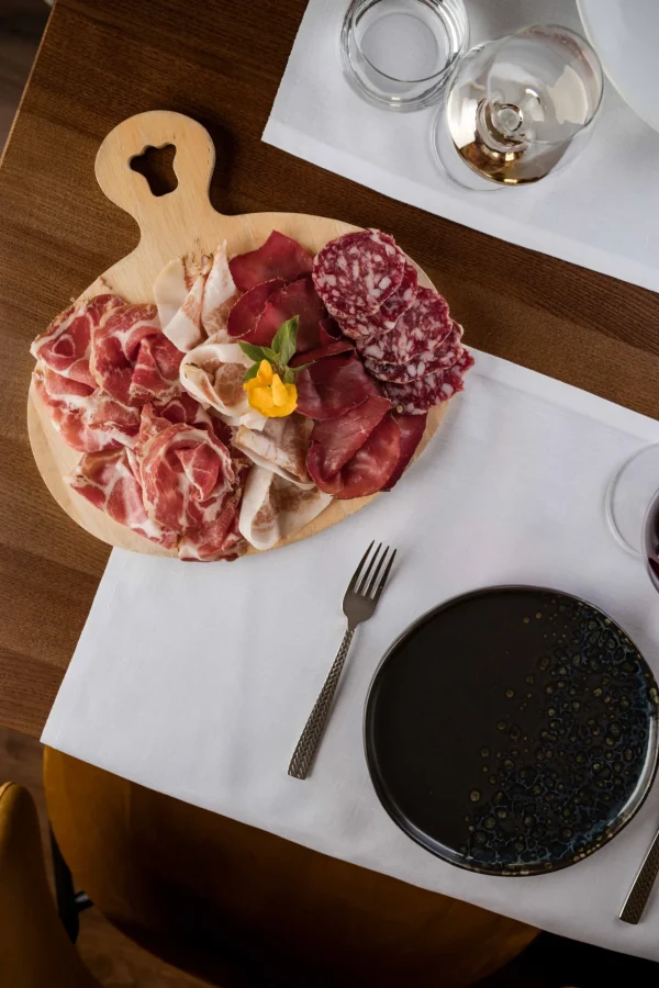 Tagliere di salumi assortiti con bicchiere di vino su tavola apparecchiata.