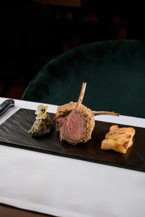 Piatto gourmet con carré di agnello, purè e patate arrosto su lavagna nera.