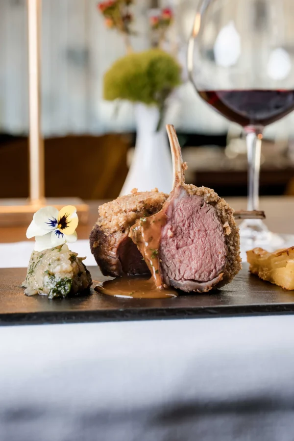 Carré di agnello al forno con contorni e bicchiere di vino rosso su tavola elegante.