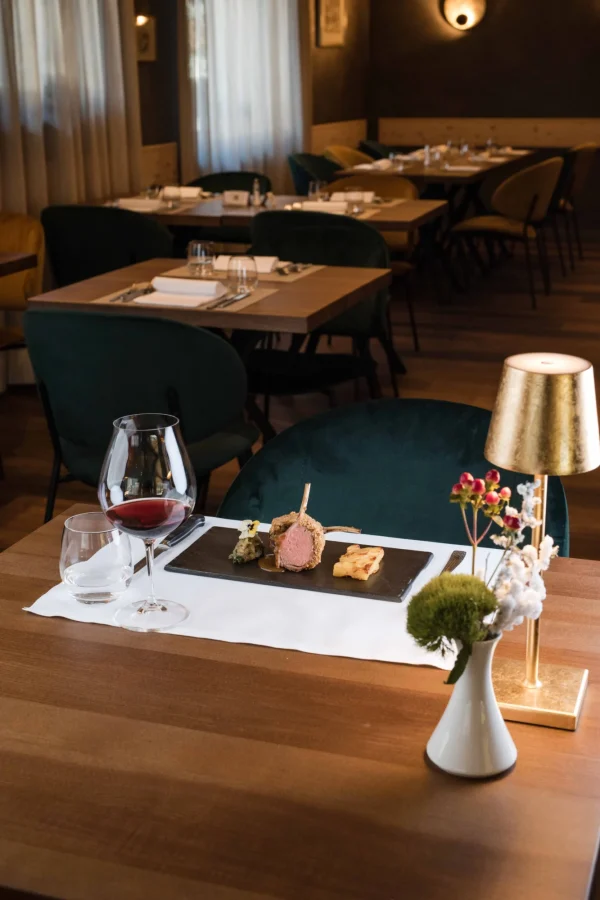 Un tavolo apparecchiato in un ristorante elegante, con un piatto gourmet e un bicchiere di vino rosso.