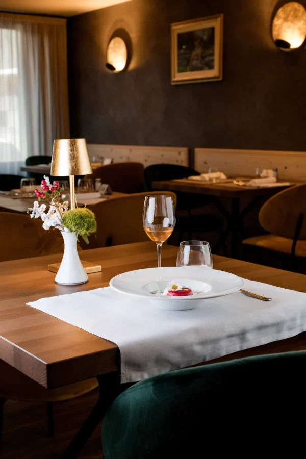 Un elegante tavolo da ristorante apparecchiato con un piatto decorato, un calice di vino e un centrotavola floreale.