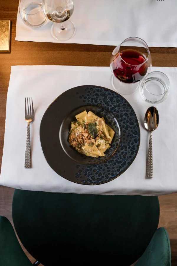 Piatto di pasta gourmet con bicchiere di vino rosso su tavola apparecchiata elegantemente.