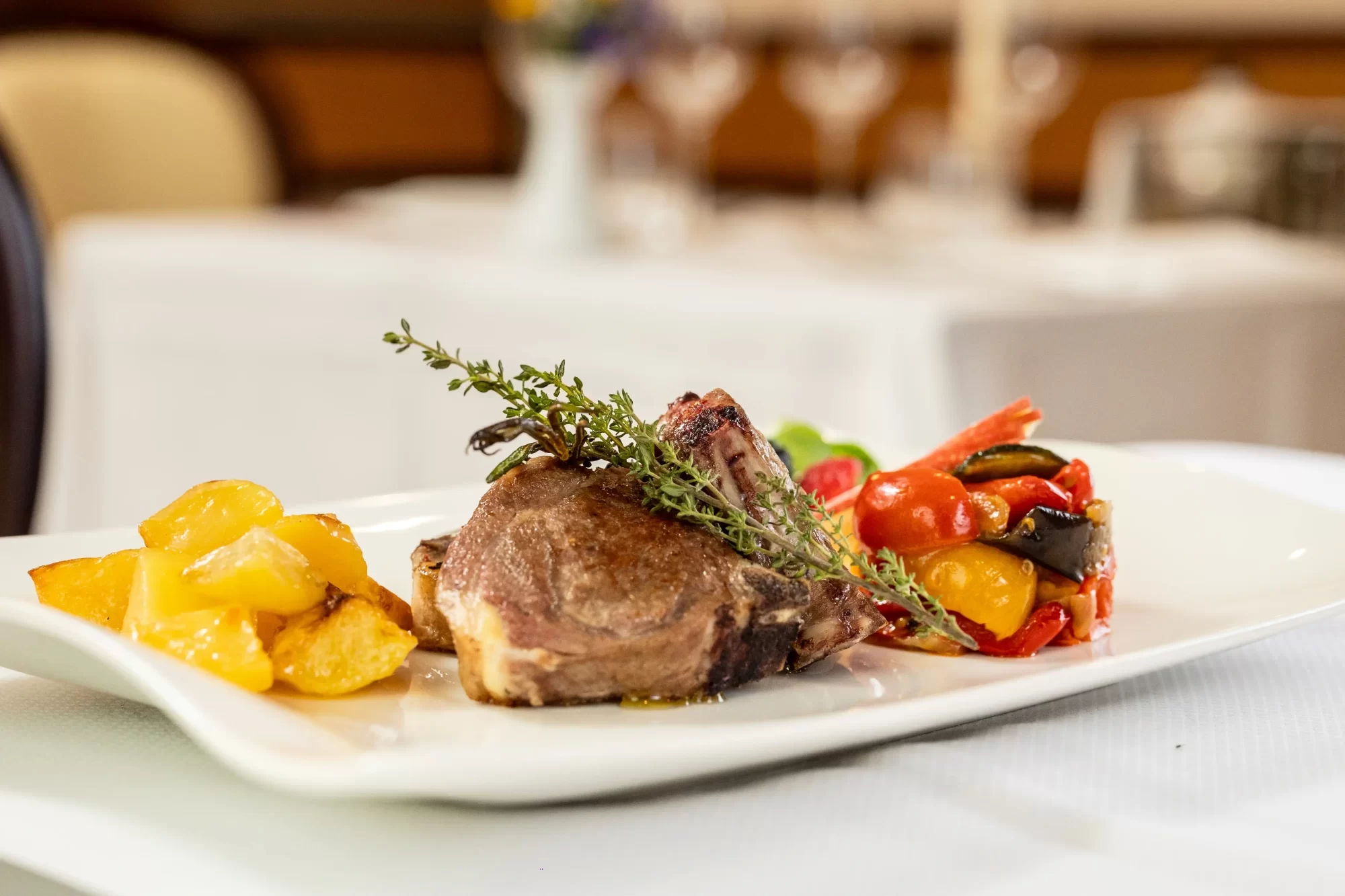 Piatto di costolette di carne con contorno di patate e verdure grigliate.