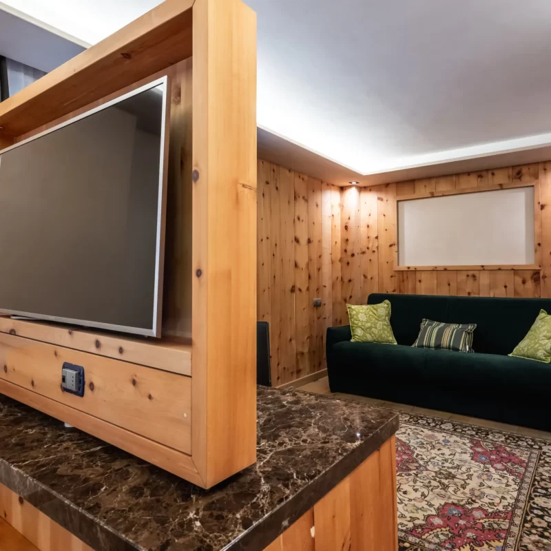 Gemütliches Wohnzimmer mit Holzwänden, grünem Sofa und modernem Fernseher.