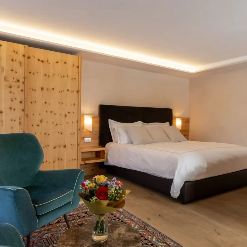 Elegantes Schlafzimmer mit Doppelbett, grünem Sessel und Holzmöbeln.