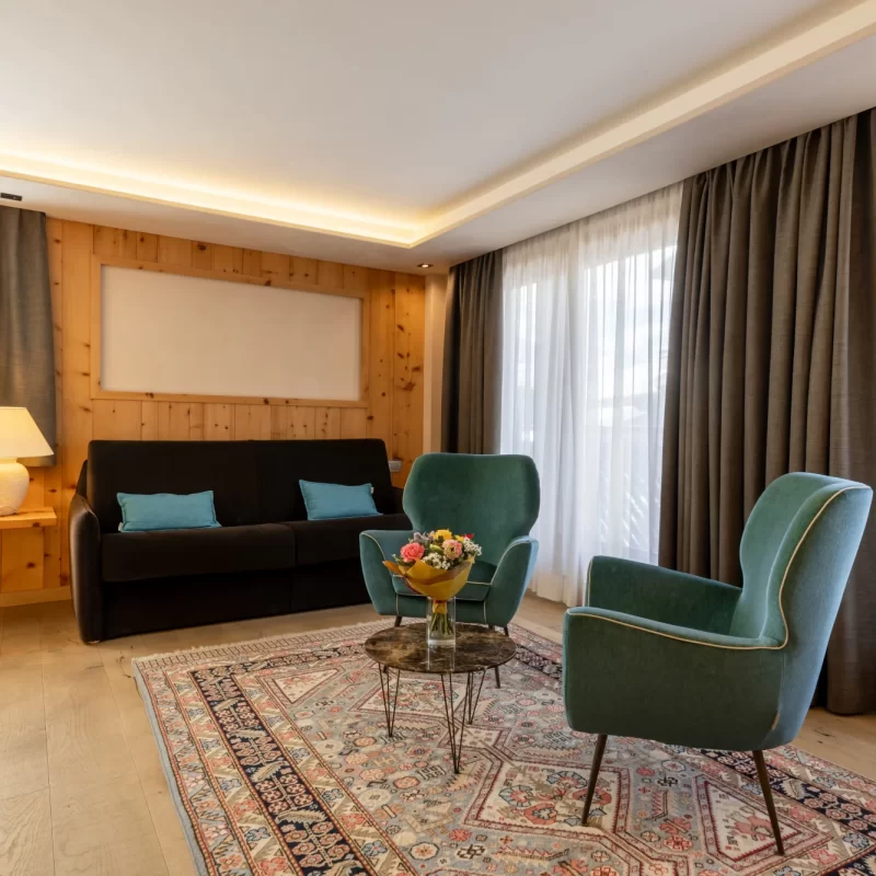 Gemütlicher Raum mit grünen Sesseln, dunklem Sofa und verziertem Teppich.