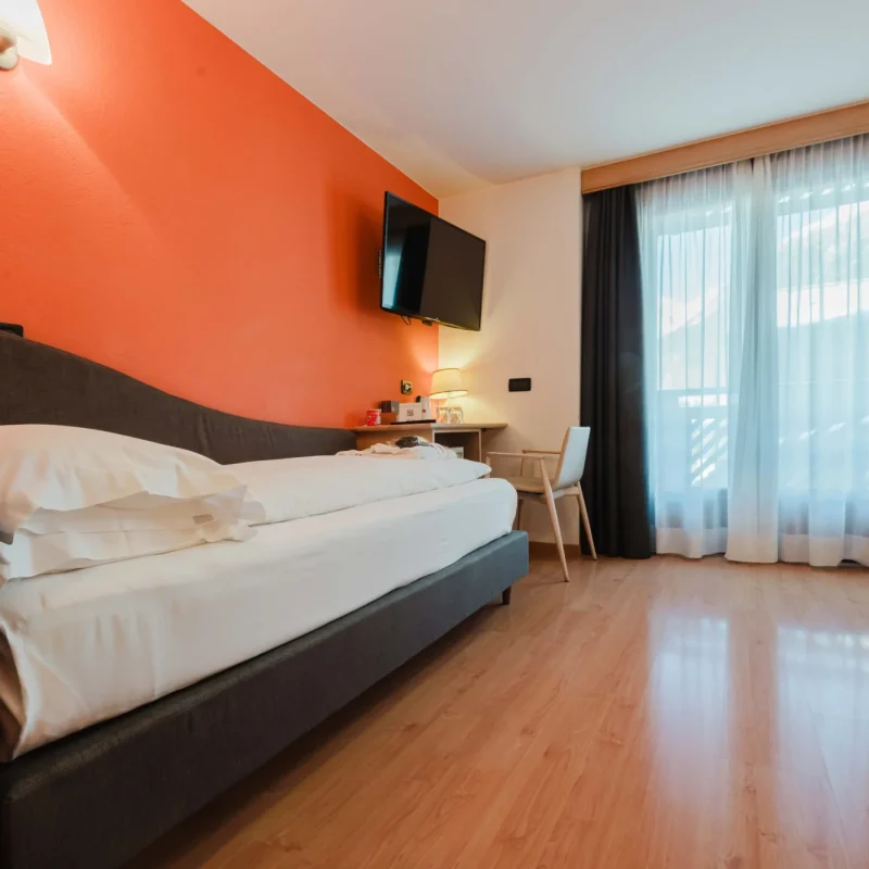 Ein gemütliches Hotelzimmer mit Doppelbett, Fernseher und großem Fenster mit Vorhängen.