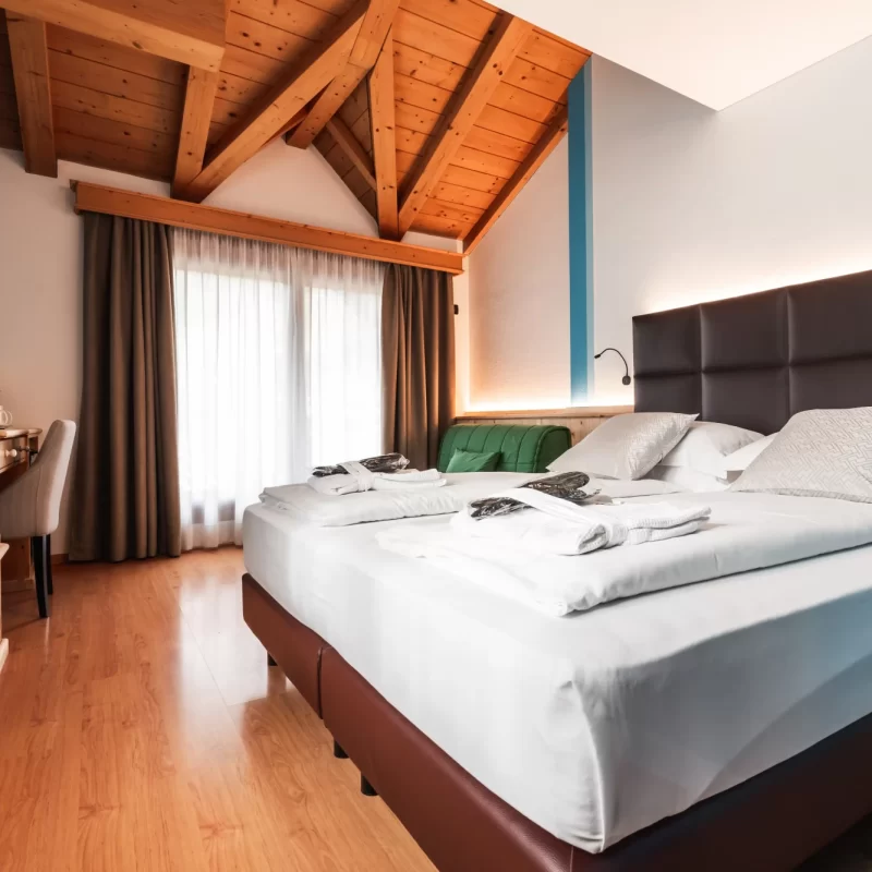 Hotelzimmer mit Doppelbett, Holzdecke und Schreibtisch am Fenster.